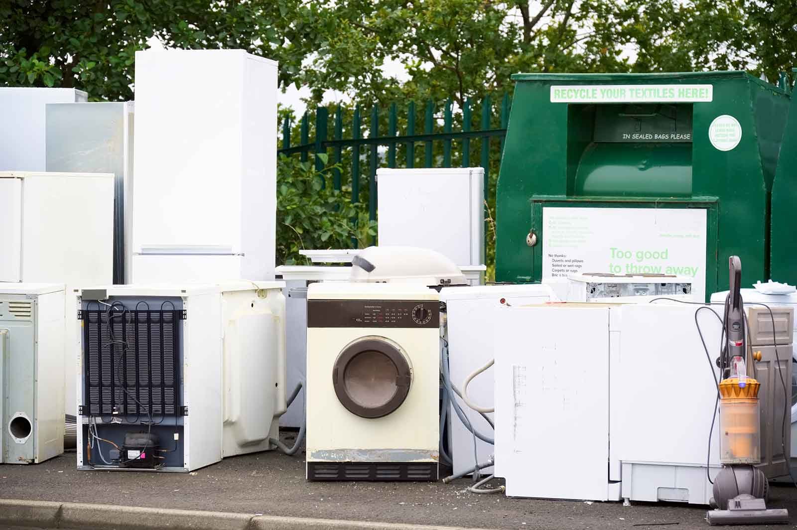 an old dishwashers, washing machines, and refrigerators outside on the curb waiting to be picked up for appliance recycling service