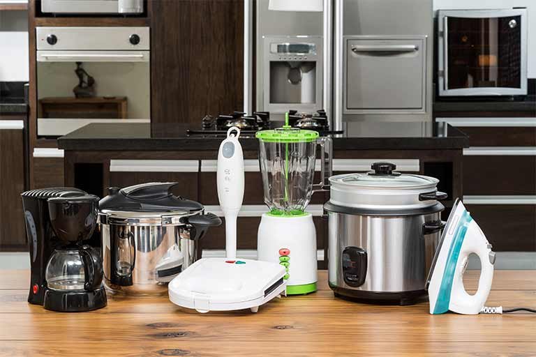 small appliances such as an old coffee maker, blender, crock pot, and iron on a kitchen table that need to be recycled