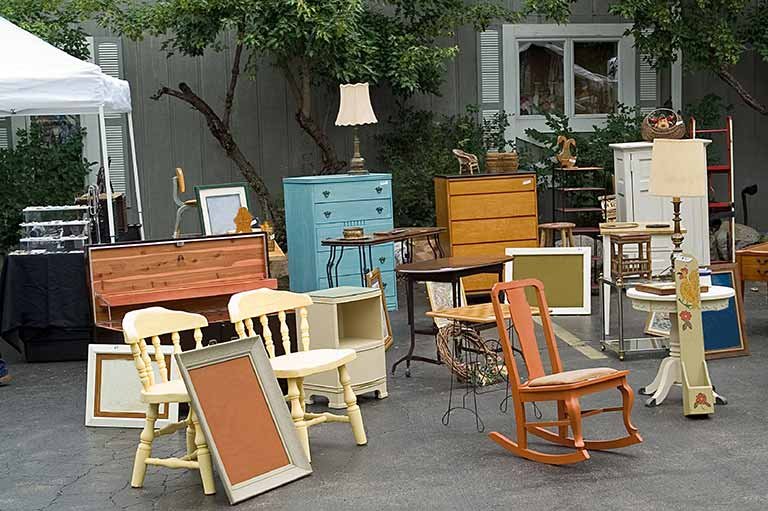 Outdoor display of assorted furniture items, including chairs, tables, and cabinets, promoting furniture resale and recycling options.