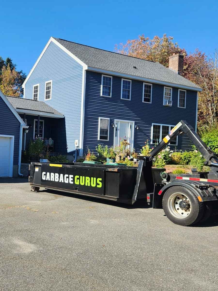 10-yard dumpster from Garbage Gurus parked in front of a blue house, showcasing residential cleanup service for junk and debris disposal.
