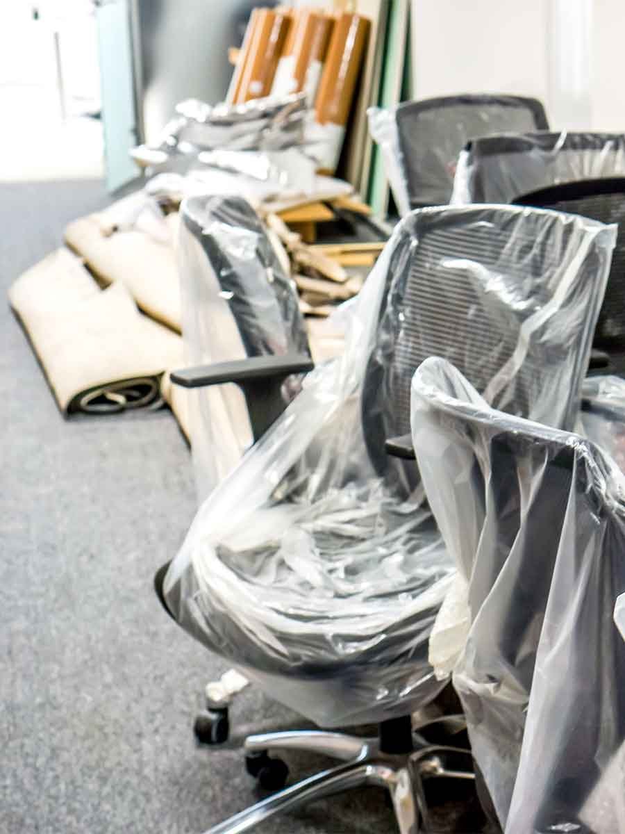 Office chairs wrapped in plastic, stacked alongside disassembled furniture, showcasing the process of office furniture removal and disposal services by Garbage Gurus.