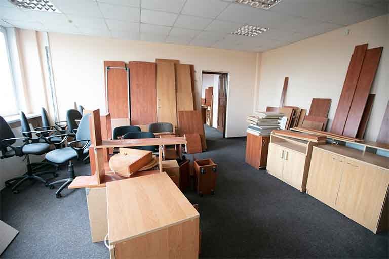 Office furniture removal scene featuring disassembled desks, chairs, and cabinets in a spacious office setting, highlighting the need for efficient disposal services by Garbage Gurus.