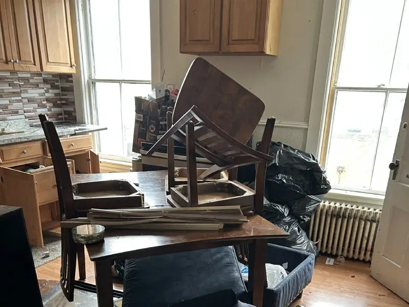 Kitchen space in an apartment with stacked broken furniture and bags of trash and other household clutter representing apartment cleanout service for home rental properties in the North Central MA region