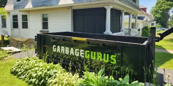 15 yard dumpster branded with the Garbage Gurus logo in a driveway representing dumpster rental service for DIY homecleanout projects in North Central MA