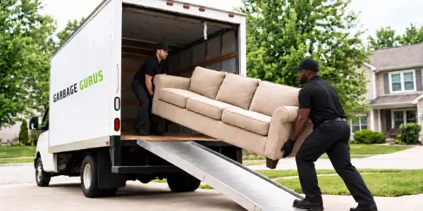 two Garbage Guru junk removal technicians loading an old couch into a box truck representing junk pickup service for residents in North Central MA